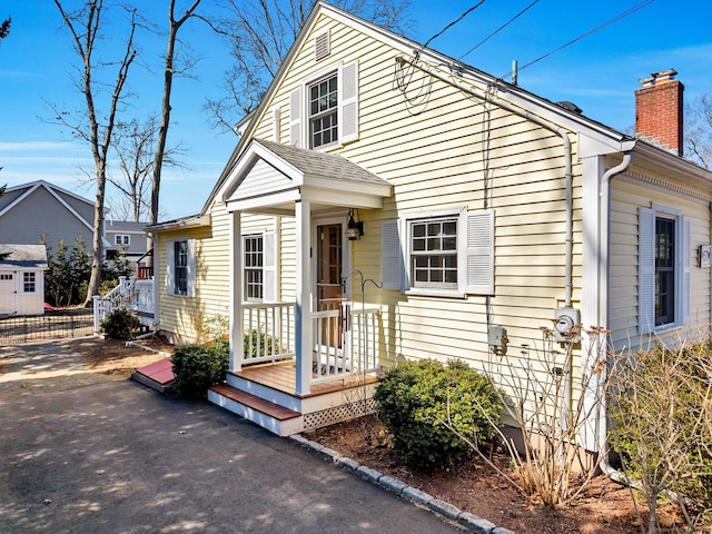 view of front facade with driveway, a chimney, and fence