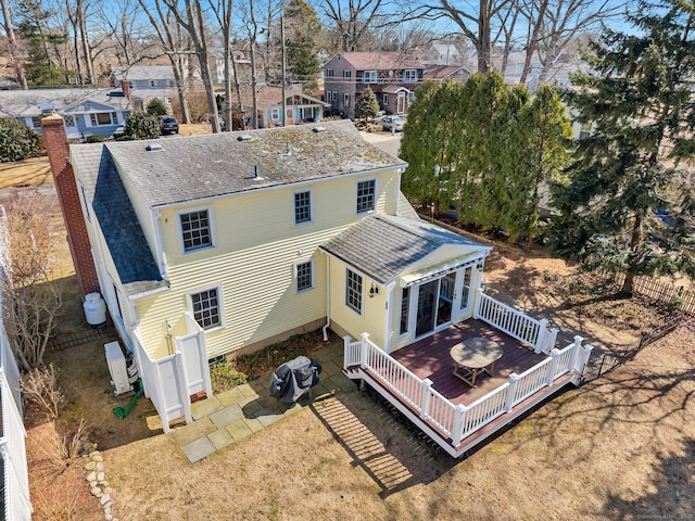 rear view of property with a deck, a lawn, and a shingled roof