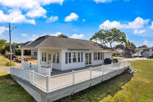 rear view of house featuring a wooden deck, a yard, and roof with shingles