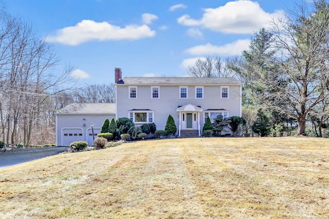 colonial home with aphalt driveway, a garage, a chimney, and a front lawn