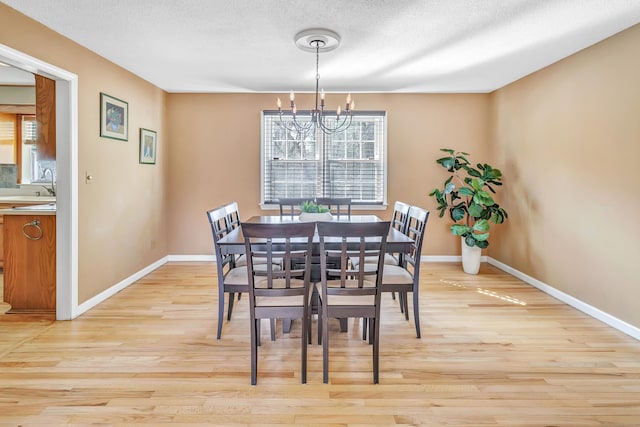 dining space featuring light wood-style flooring, a notable chandelier, baseboards, and a textured ceiling