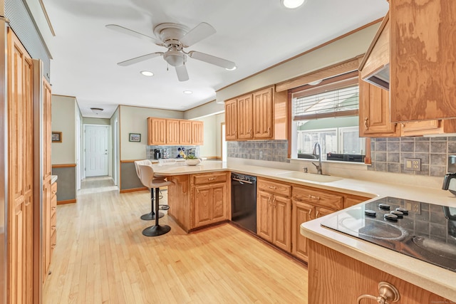 kitchen with a breakfast bar area, a sink, black appliances, light countertops, and light wood-style floors