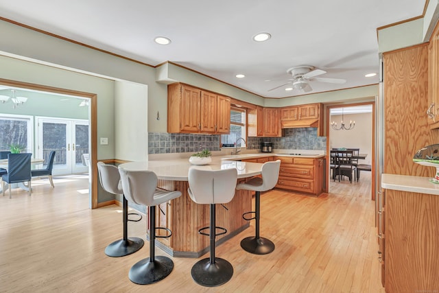 kitchen featuring light countertops, decorative backsplash, ceiling fan with notable chandelier, a kitchen breakfast bar, and light wood-style floors