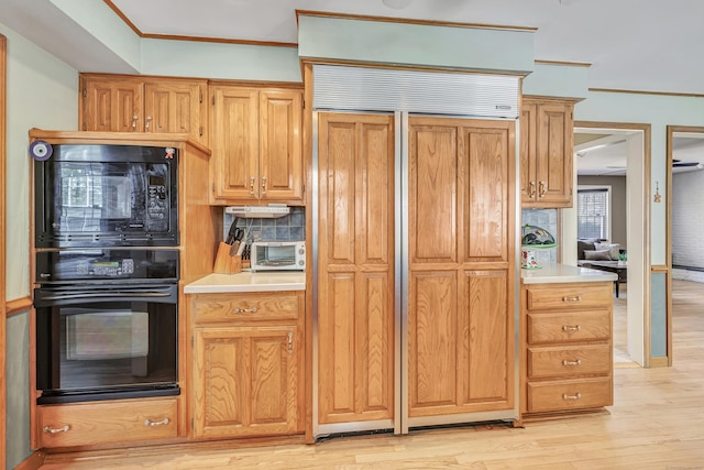 kitchen featuring backsplash, light countertops, ornamental molding, light wood-style floors, and black appliances