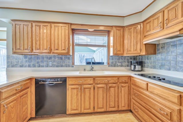 kitchen with tasteful backsplash, light wood-type flooring, light countertops, black appliances, and a sink