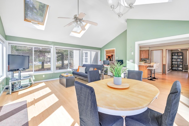 dining room with light wood-style flooring, high vaulted ceiling, a skylight, and a ceiling fan