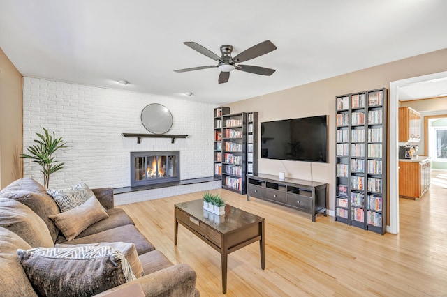 living room featuring light wood-type flooring, brick wall, ceiling fan, and a fireplace