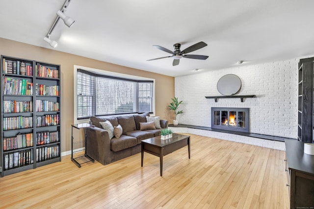 living area with a fireplace, hardwood / wood-style flooring, a ceiling fan, and brick wall