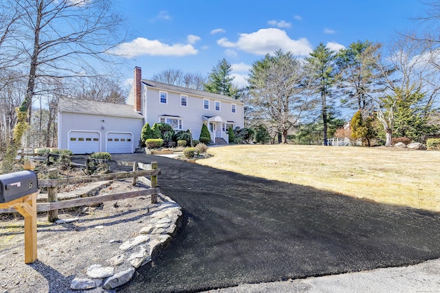 view of front of house with an attached garage, a chimney, a front lawn, an outdoor structure, and aphalt driveway