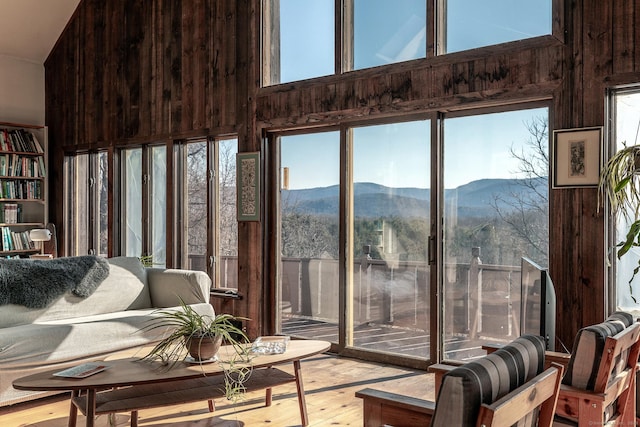 living room featuring light wood-style flooring, wood walls, a towering ceiling, and a mountain view