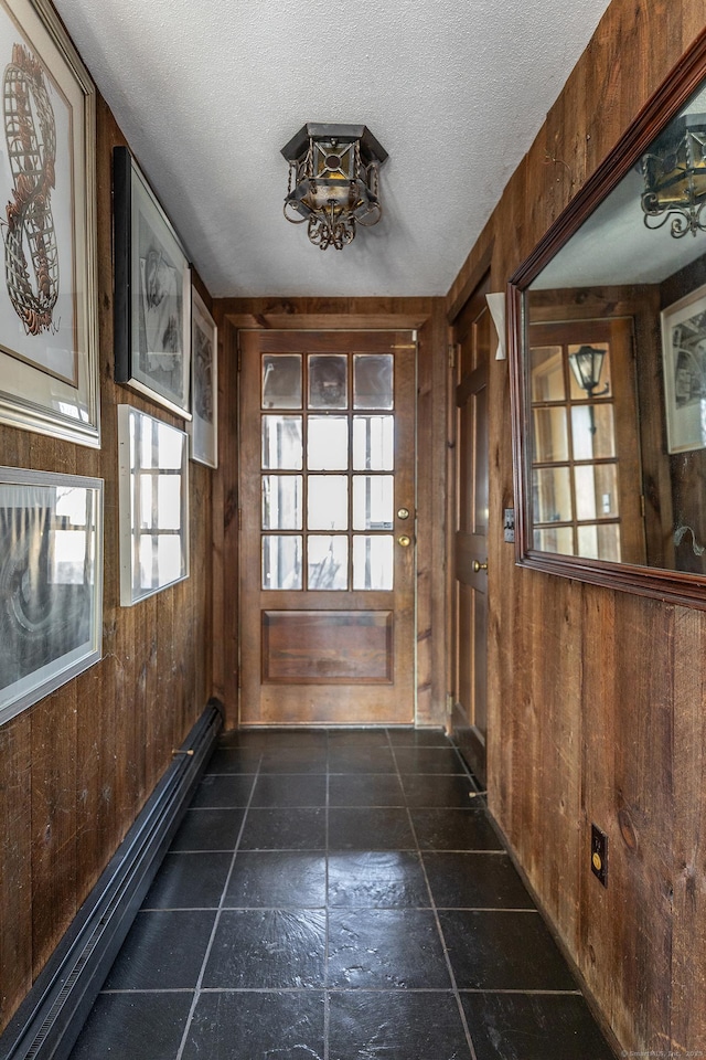 doorway with wooden walls, a textured ceiling, and a baseboard heating unit