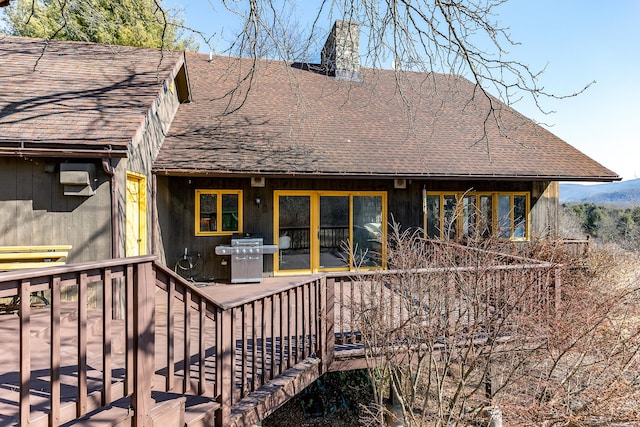 back of property with a deck, roof with shingles, and a chimney