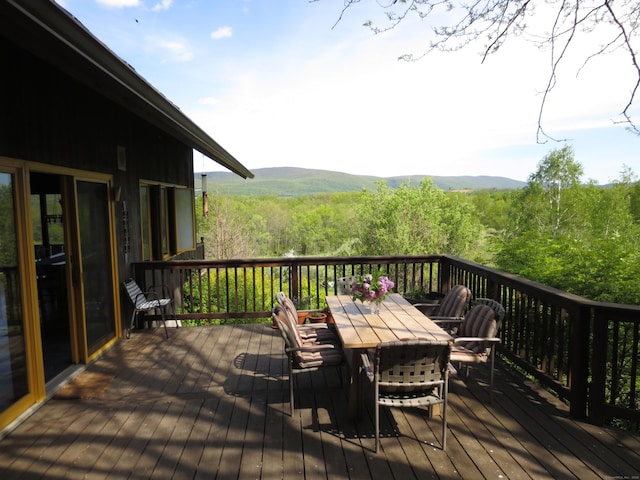 deck featuring a wooded view, outdoor dining area, and a mountain view