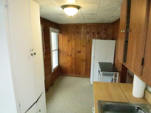 kitchen featuring wooden walls, freestanding refrigerator, and a sink