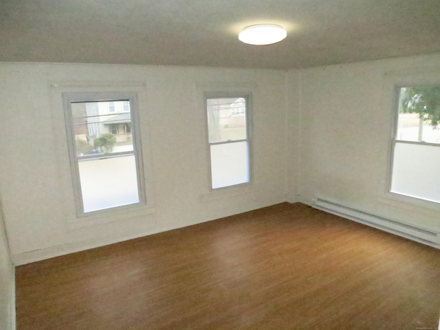 spare room featuring a baseboard heating unit, wood finished floors, and a healthy amount of sunlight