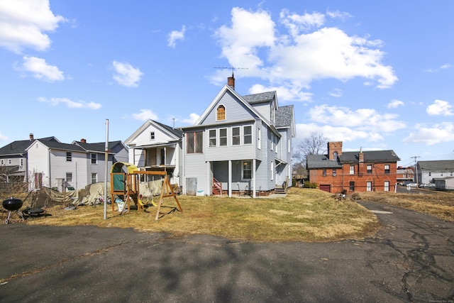 exterior space with aphalt driveway, a chimney, a playground, and a front lawn