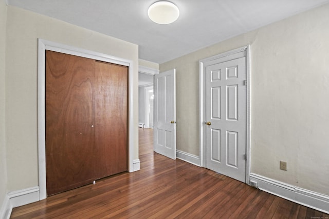 unfurnished bedroom with a closet, a baseboard radiator, baseboards, and hardwood / wood-style floors