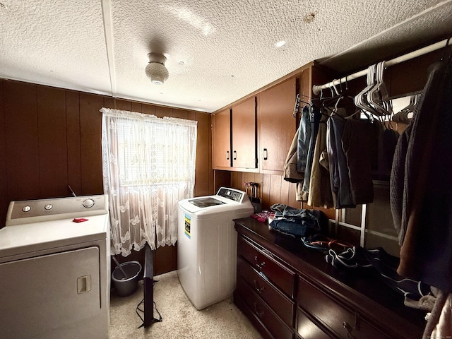 laundry room with washing machine and dryer, cabinet space, a textured ceiling, and wooden walls