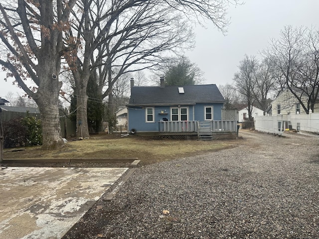 back of house featuring a chimney, gravel driveway, a deck, and fence