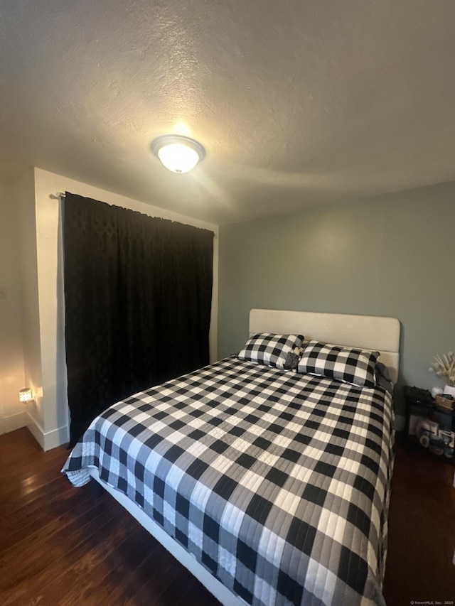 bedroom featuring baseboards, a textured ceiling, and wood finished floors