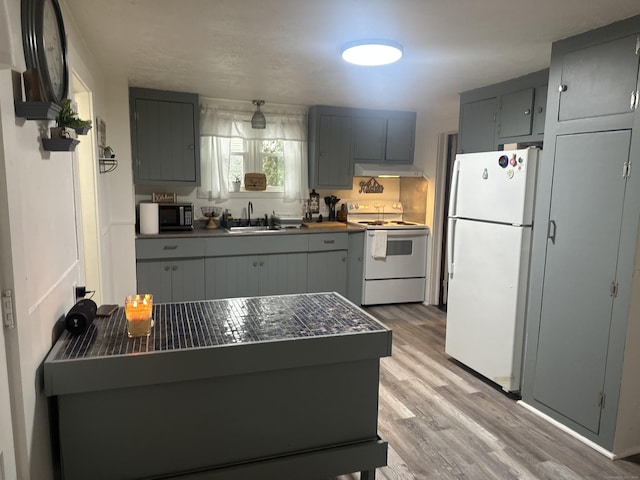 kitchen featuring white appliances, a sink, gray cabinetry, under cabinet range hood, and dark countertops