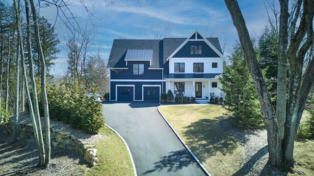 modern inspired farmhouse featuring an attached garage, a front yard, covered porch, driveway, and a standing seam roof