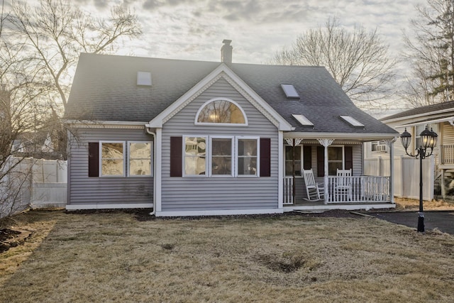 rear view of property with a lawn, a porch, a chimney, and fence