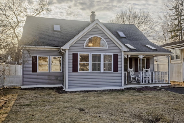 rear view of property featuring fence, roof with shingles, a porch, a yard, and a chimney