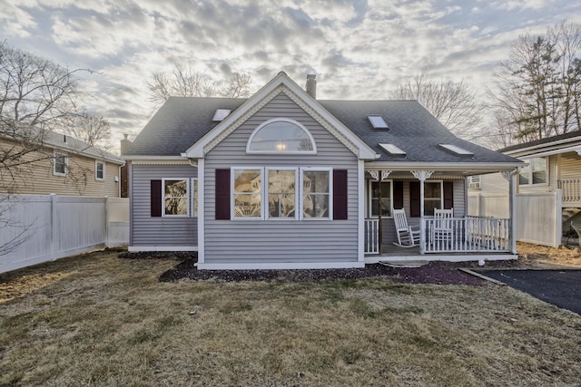 rear view of house featuring a lawn, a porch, fence, a shingled roof, and a chimney