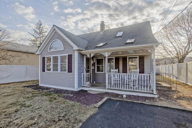 view of front of home with covered porch, a chimney, roof with shingles, and fence