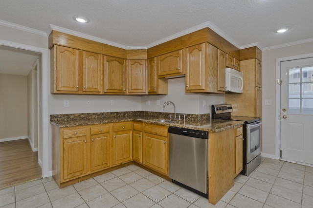 kitchen featuring ornamental molding, a sink, dark stone counters, appliances with stainless steel finishes, and light tile patterned floors