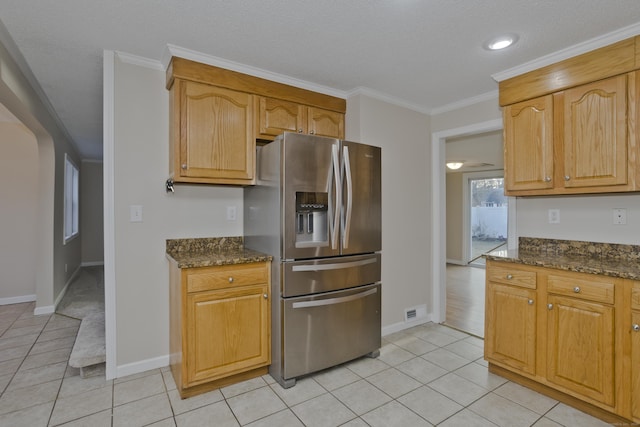 kitchen with visible vents, crown molding, light tile patterned floors, dark stone countertops, and stainless steel fridge