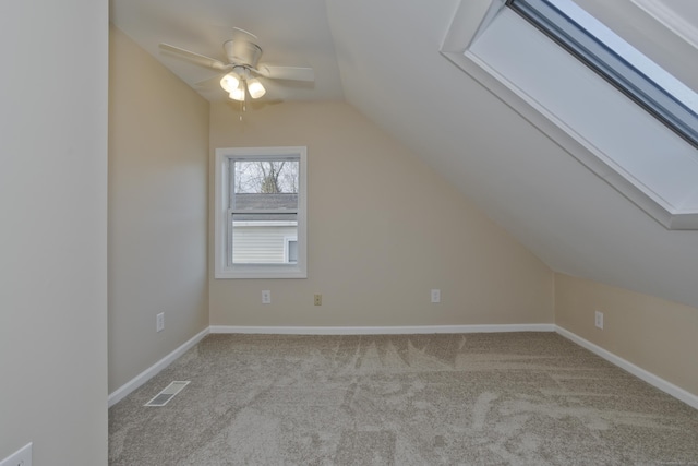 additional living space featuring visible vents, baseboards, ceiling fan, lofted ceiling with skylight, and carpet floors