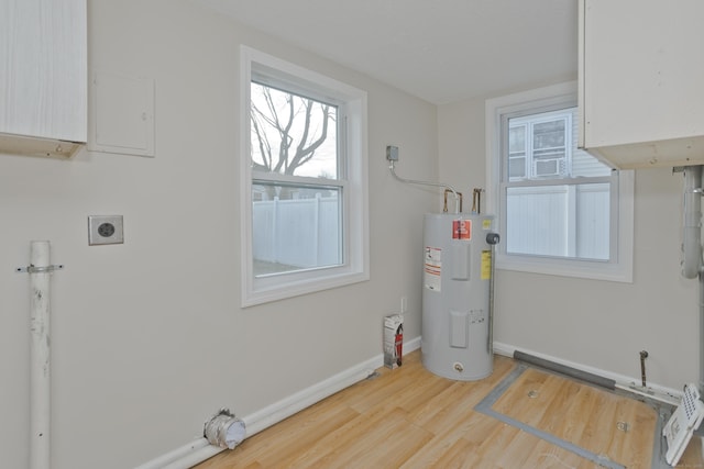 laundry area with electric dryer hookup, electric water heater, wood finished floors, cabinet space, and baseboards