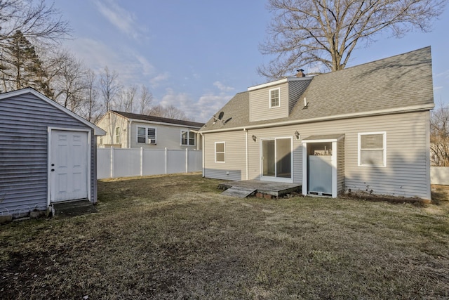 back of property with an outdoor structure, a shingled roof, a yard, and fence