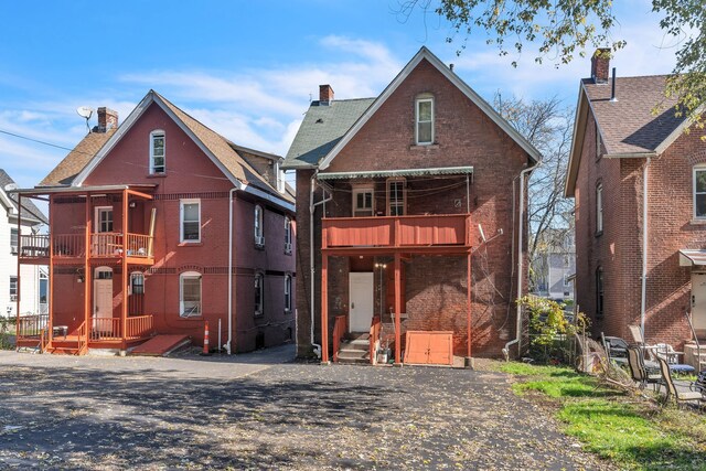 back of house with a balcony, brick siding, and a chimney