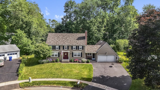 colonial home featuring an attached garage, a shingled roof, a front yard, a chimney, and driveway