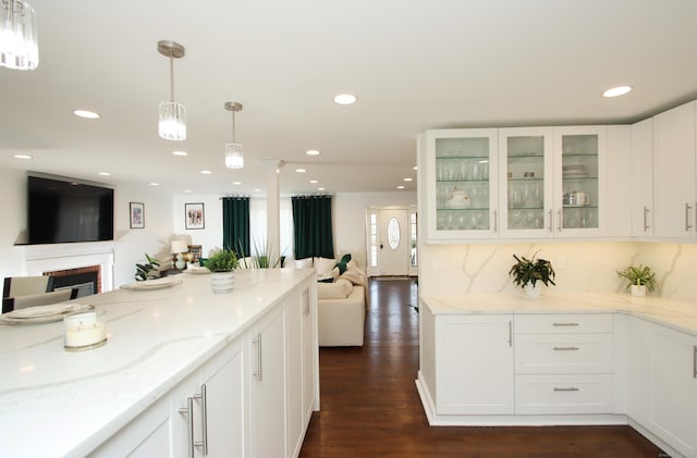 kitchen with glass insert cabinets, open floor plan, light stone counters, white cabinetry, and dark wood-style flooring