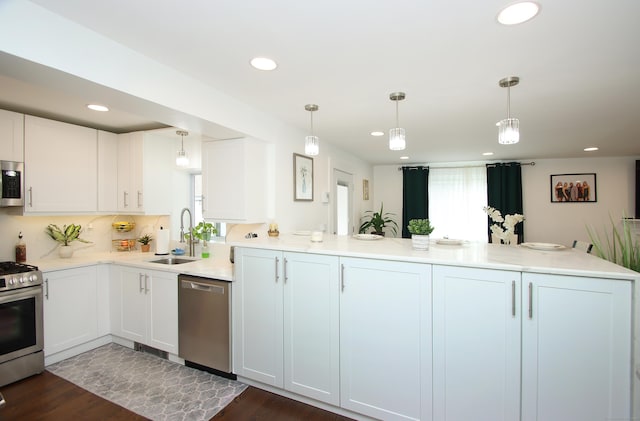 kitchen featuring a peninsula, a sink, decorative backsplash, stainless steel appliances, and decorative light fixtures