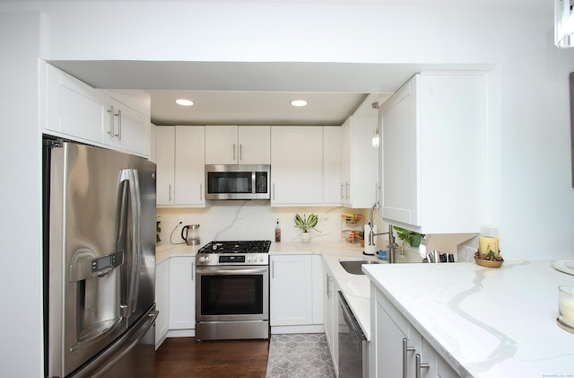 kitchen with light stone countertops, decorative backsplash, appliances with stainless steel finishes, white cabinetry, and a sink