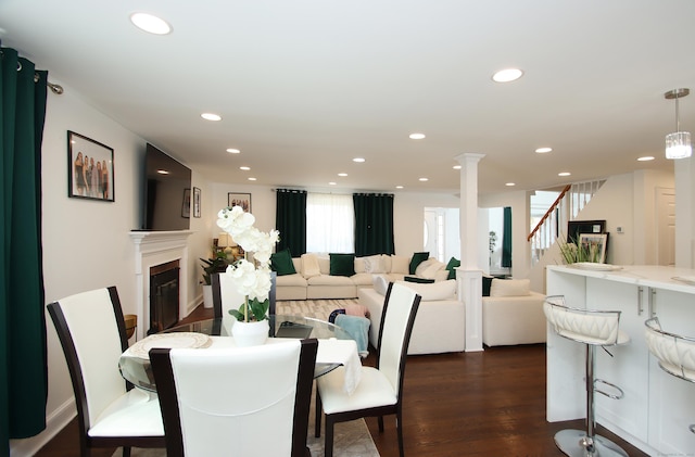 dining area with a glass covered fireplace, dark wood finished floors, recessed lighting, decorative columns, and stairs