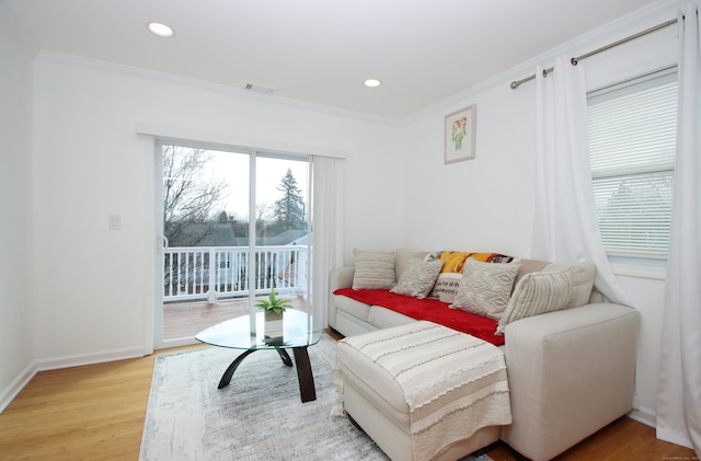 living area with visible vents, baseboards, light wood-style flooring, and ornamental molding