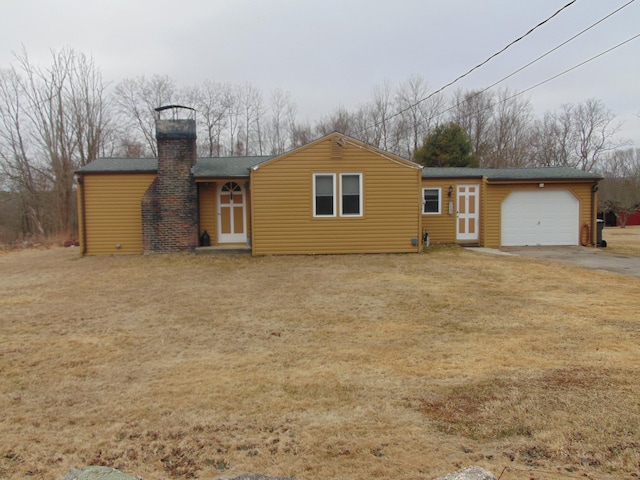 back of house with a yard, an attached garage, a chimney, and roof with shingles