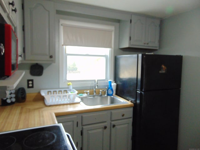 kitchen with a sink, light countertops, freestanding refrigerator, white cabinets, and range