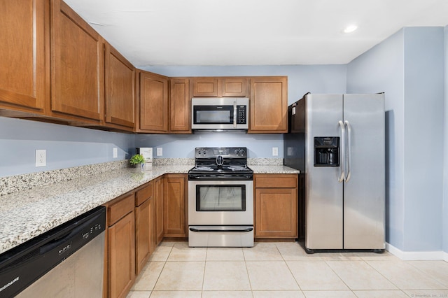 kitchen with stainless steel appliances, light stone countertops, light tile patterned floors, and brown cabinets
