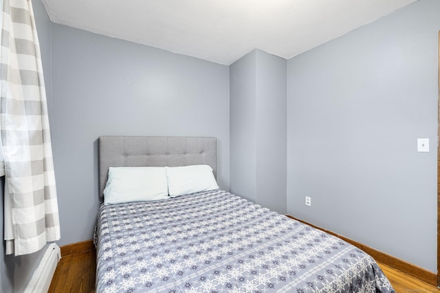 bedroom with wood finished floors, a baseboard heating unit, and baseboards