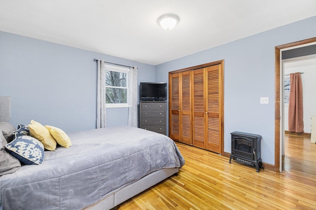 bedroom with light wood-type flooring, a closet, a wood stove, and baseboards
