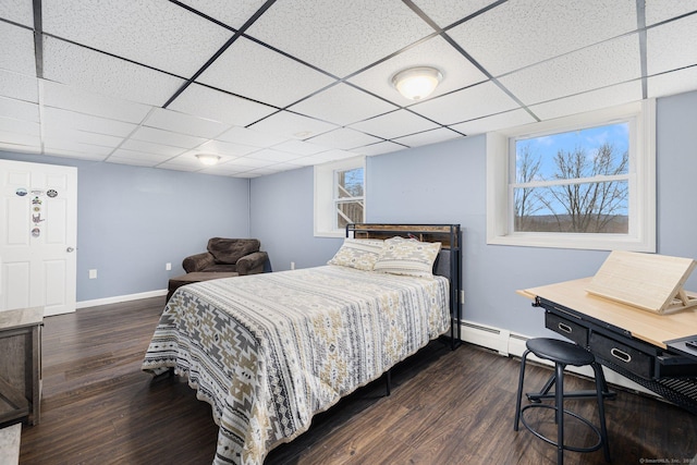 bedroom featuring a drop ceiling, a baseboard radiator, baseboards, and dark wood finished floors