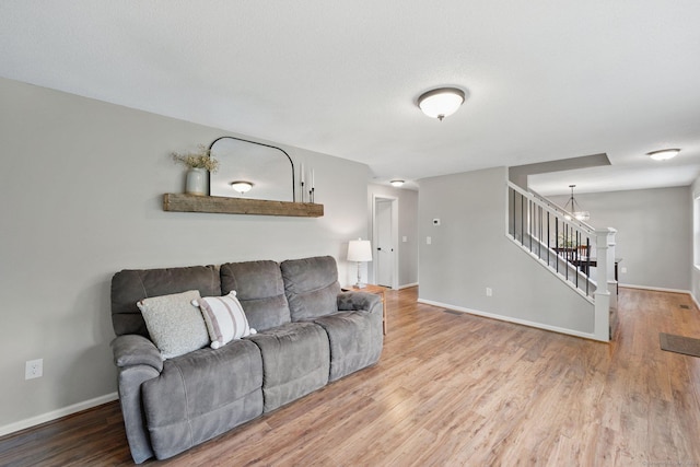 living area with a chandelier, wood finished floors, baseboards, and stairs
