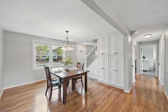 dining space featuring a textured ceiling, a chandelier, baseboards, light wood finished floors, and stairway